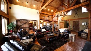 A spacious living room with leather sofas, a coffee table, and a fireplace. There is a wooden ceiling with exposed beams and a chandelier. - Fly Fisherman's Lodge on the Bitterroot River,  Lolo Mt (Lolo)