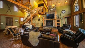 A spacious living room with a fireplace, leather sofas, a wooden staircase, and a large TV. - Fly Fisherman's Lodge on the Bitterroot River,  Lolo Mt (Lolo)