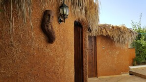 Um edifício rústico com telhado de palha, porta de madeira e luminária na parede.