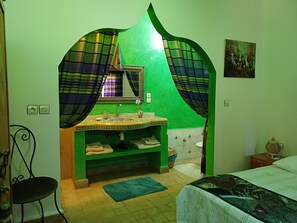 Une salle de bain avec un mur vert, un lavabo agrémenté d’un miroir décoratif et un porte-serviettes.