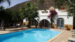 Uma área de piscina com piscina azul límpida, rodeada por espreguiçadeiras e um muro de pedra.