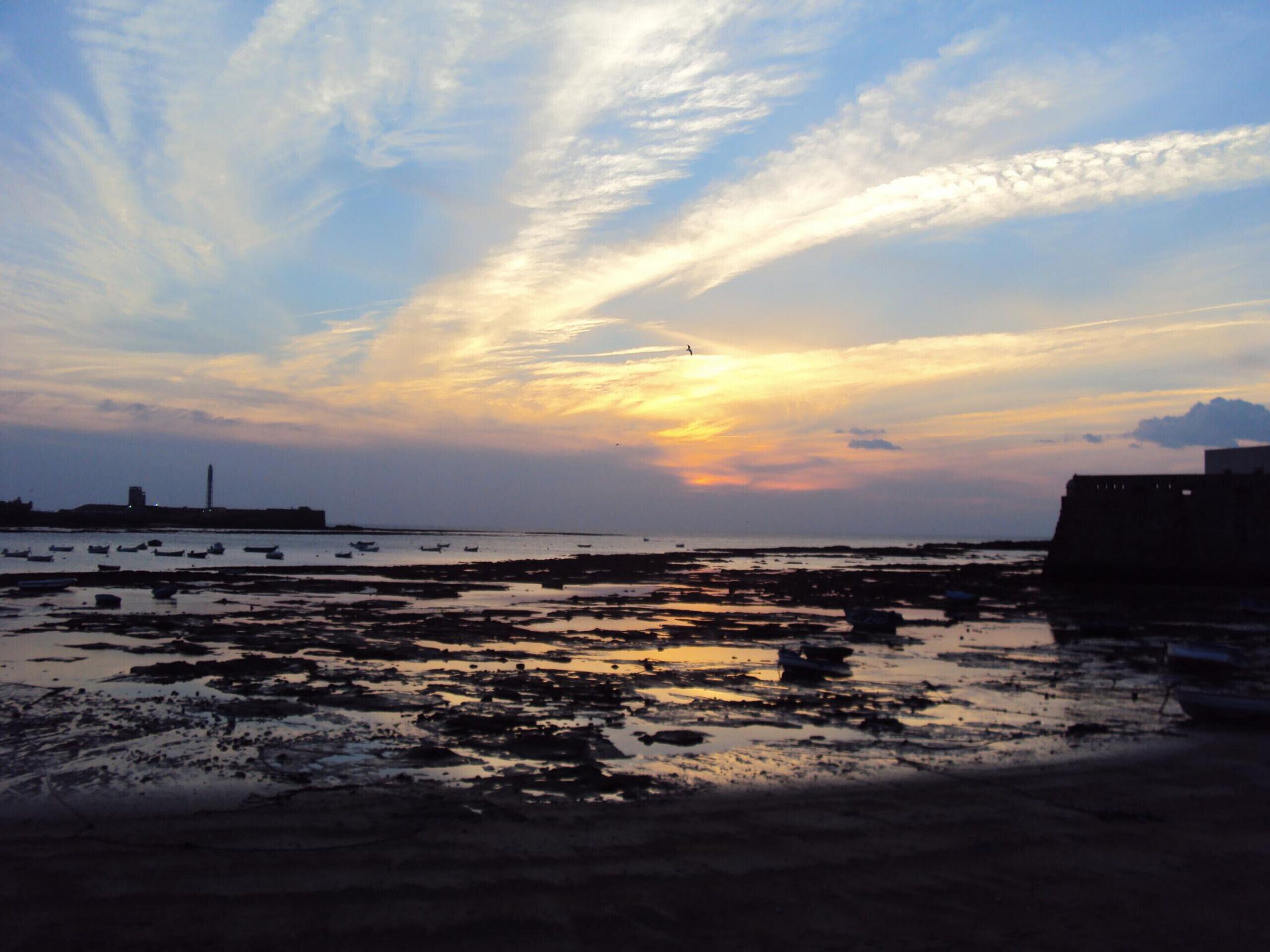 A coastal sunset with boats on the water and a distant cityscape.
