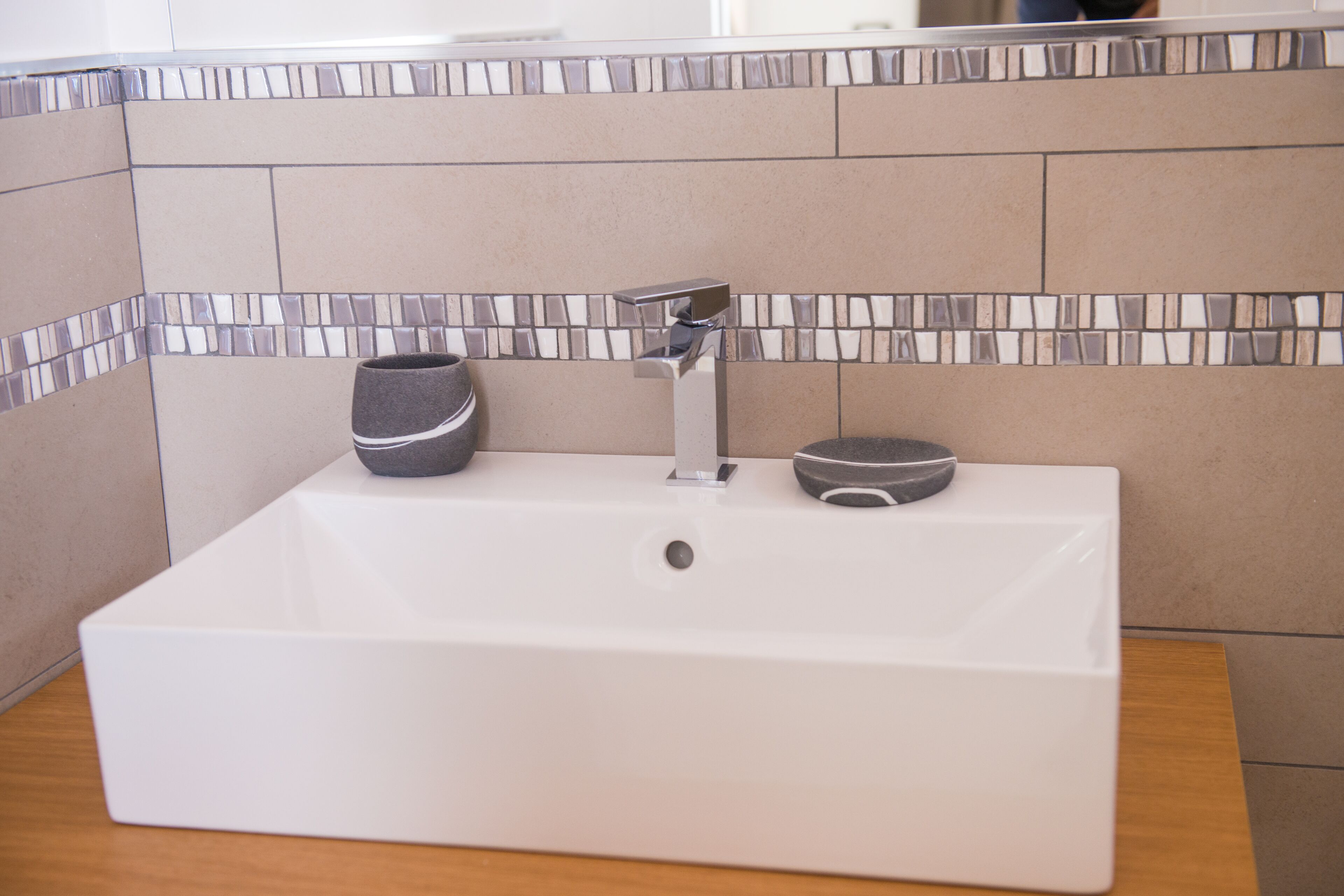 Ein weißes, rechteckiges Waschbecken mit einem modernen Wasserhahn und zwei schwarzen Seifenschalen.