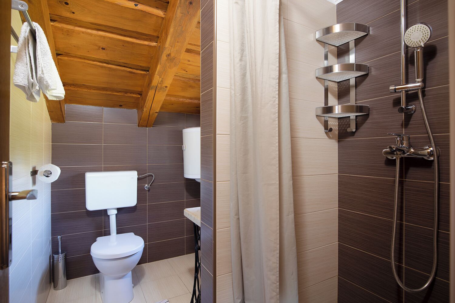 A bathroom with a wooden ceiling, a toilet, a shower with multiple heads, and a towel rack.
