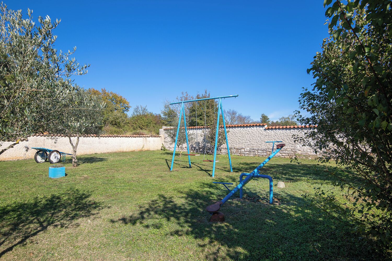 Ein Garten mit Schaukel, einem kleinen blauen Wagen und einer Steinmauer.