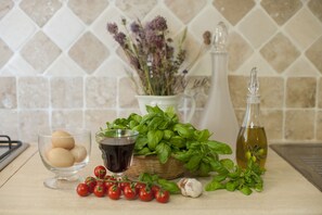 A kitchen counter with eggs, tomatoes, basil, garlic, olive oil, and a bottle of vinegar.