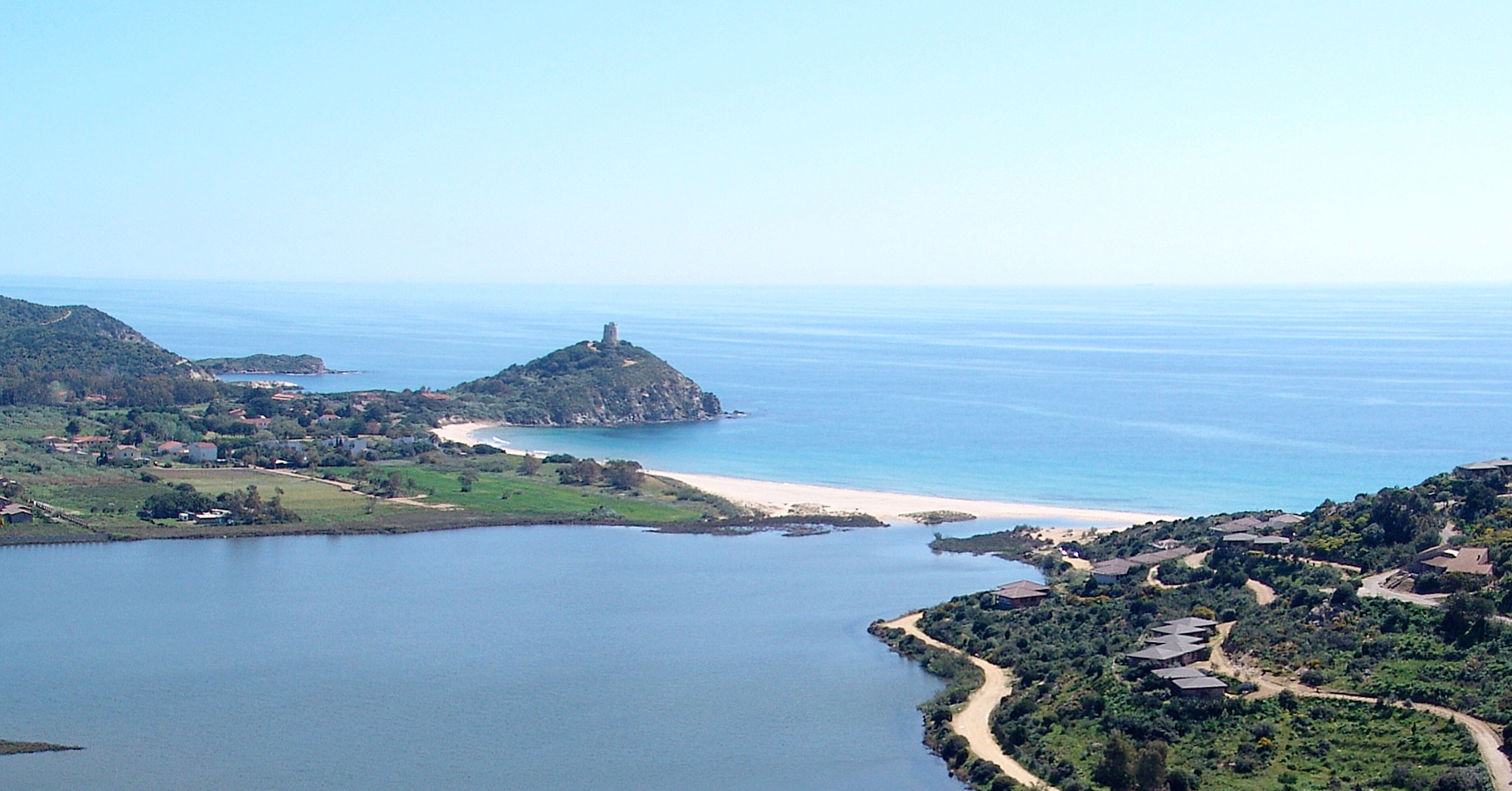 An aerial view of a coastal area with a prominent hilltop structure, a beach, and surrounding greenery.