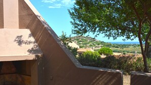 Une vue depuis un balcon doté d’une structure en pierre, donnant sur une colline parsemée de bâtiments et de verdure.