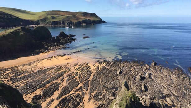 A coastal landscape with a sandy beach, rocky outcrops, and calm sea.