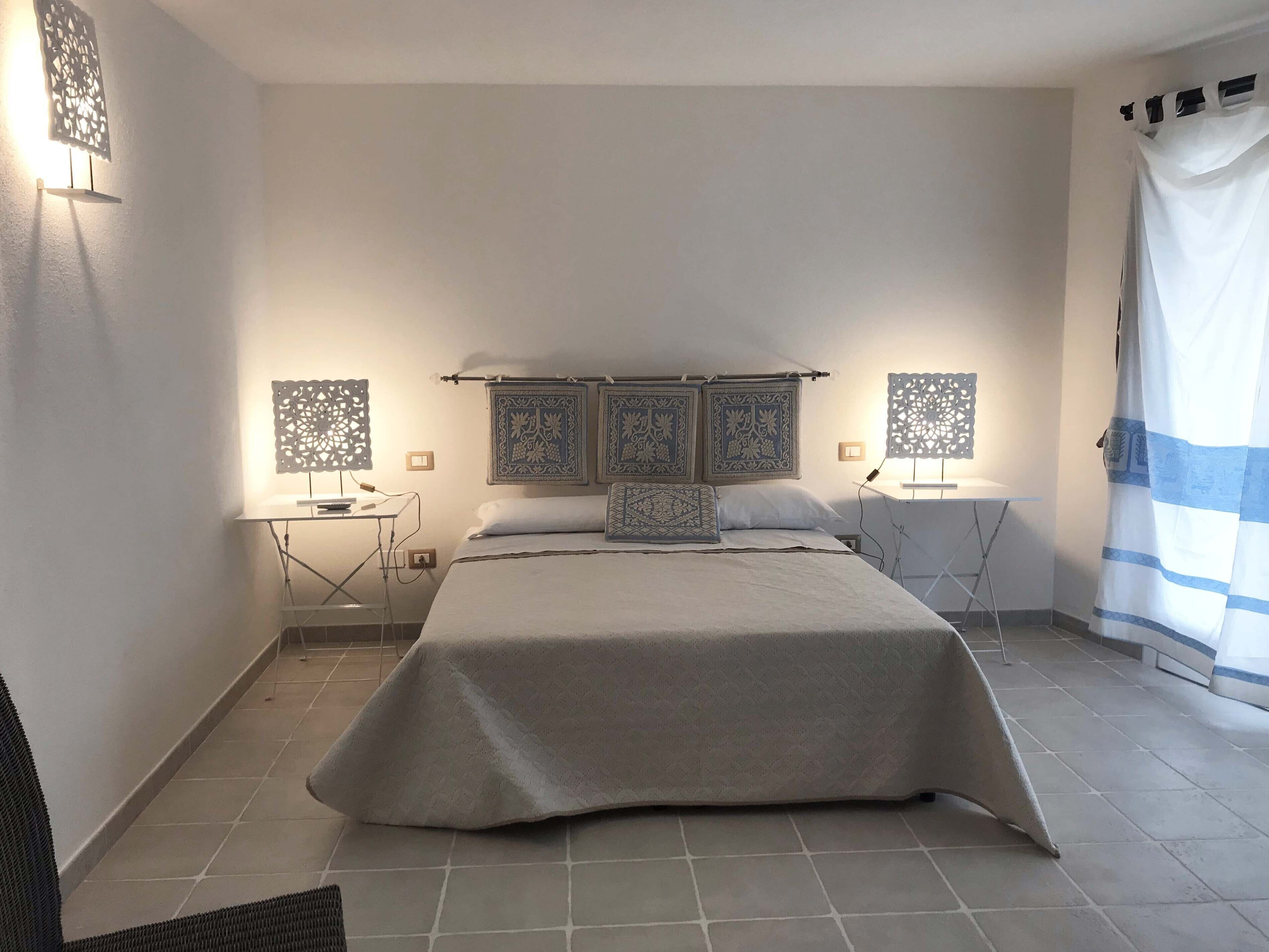 Quarto bem arrumado com cama, mesas de cabeceira e painéis decorativos na parede.