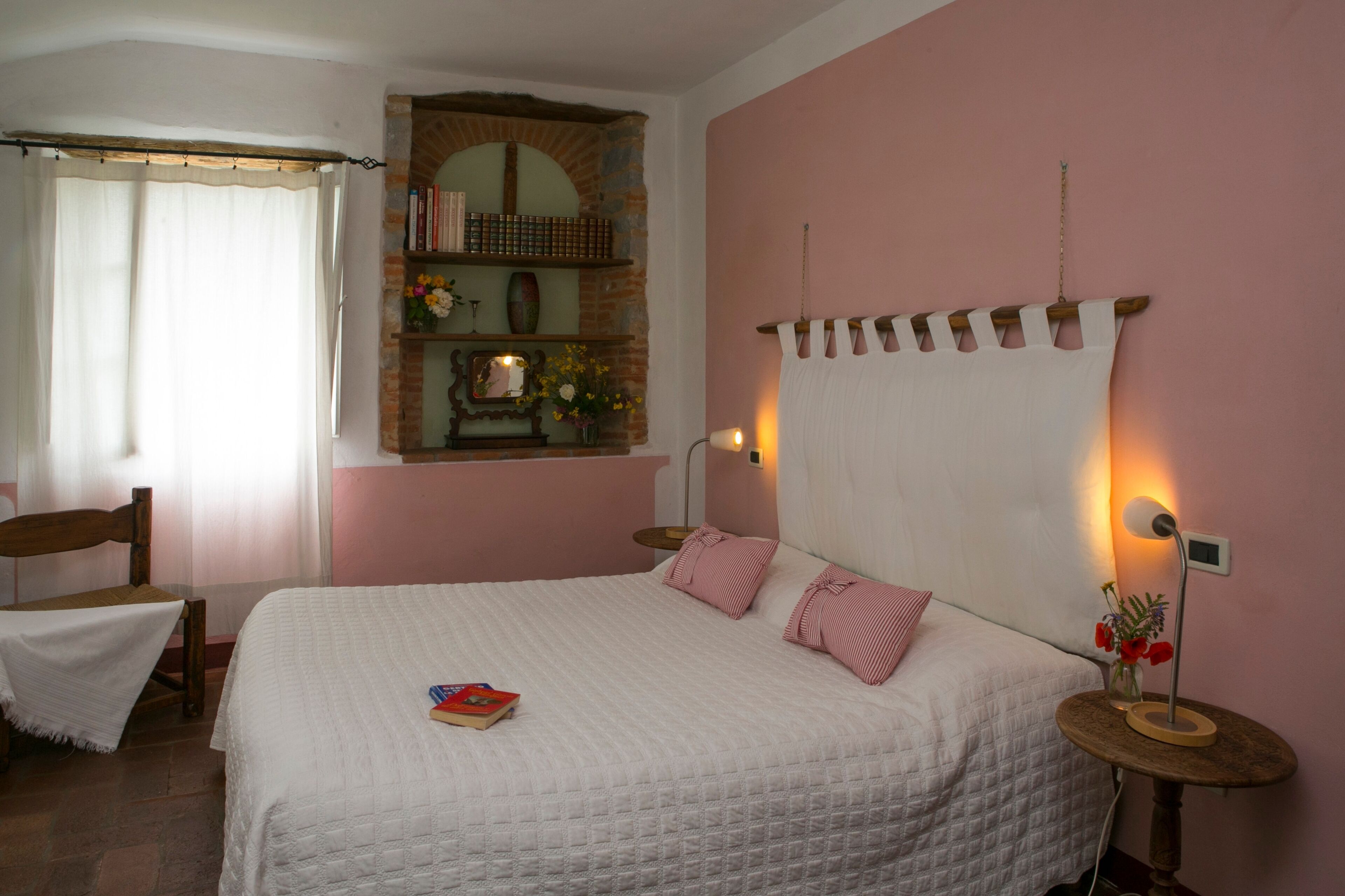 Ein Schlafzimmer mit einem großen Bett, einem Holzstuhl, einem kleinen Tisch mit einer Lampe und einem Bücherregal.