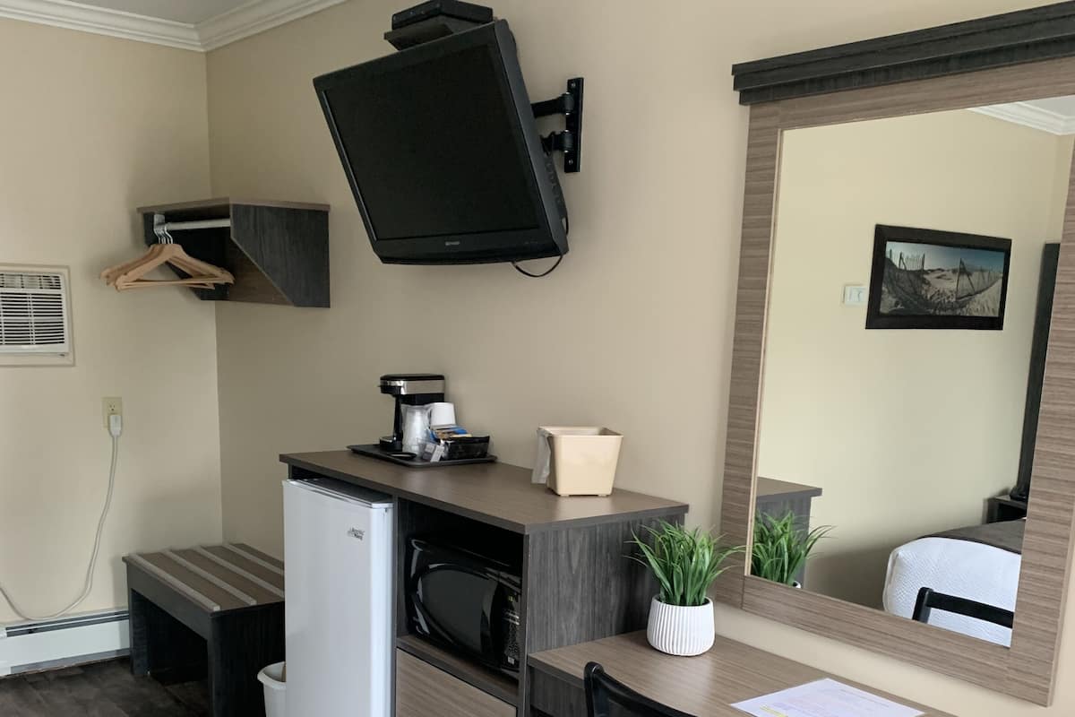 Une chambre d’hôtel compacte comprenant un coin cuisine, un téléviseur à écran plat fixé au mur, un petit bureau avec une chaise et un miroir qui reflète une partie de la pièce.