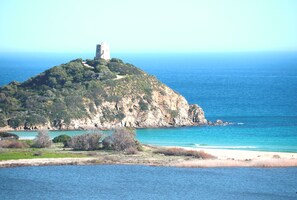 Un paisaje costero con una colina rocosa destacada que presenta una estructura parecida a una torre.