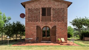 Ein Backsteinhaus mit Satellitenschüssel, zwei Türen und einer Terrasse mit Stühlen und Tisch.