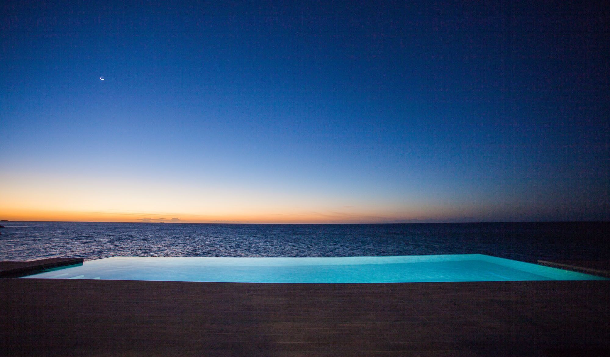 A poolside view at sunset with a clear sky and calm sea.