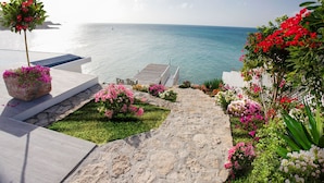A stone pathway leading to a wooden deck overlooking a body of water. - BEAUTIFUL SUNSET OCEANFRONT VILLA WITH INFINITY POOL (Crosbies)