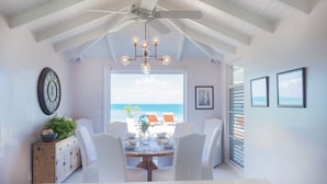 A dining area with a view of the ocean, white furniture, and a ceiling fan. - BEAUTIFUL SUNSET OCEANFRONT VILLA WITH INFINITY POOL (Crosbies)