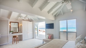A bedroom with a large bed, a desk with a chair, a wardrobe, and a view of the beach. - BEAUTIFUL SUNSET OCEANFRONT VILLA WITH INFINITY POOL (Crosbies)