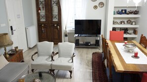 Un salón con dos sillones, una mesa de comedor de madera, un televisor y estantes con adornos.