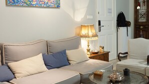 Una sala de estar con un sofá, una mesa de centro y una lámpara. Se observa una puerta y un perchero al fondo.