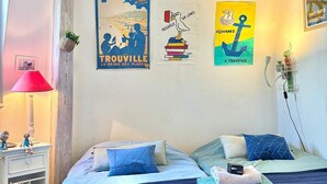 A bedroom with two beds, a nightstand, a lamp, and wall art. - Charming and authentic fisherman's house, downtown and near the beach (Trouville-sur-Mer)