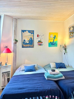 A bedroom with two beds, a nightstand, a lamp, and wall art.