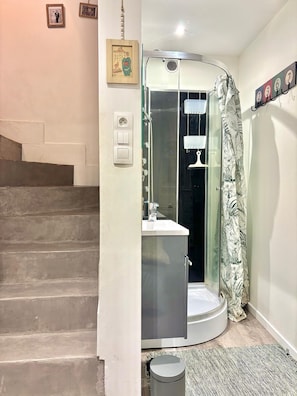 A bathroom with a shower, a sink, and a toilet. There is a staircase leading to another room.