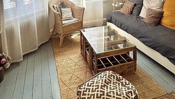 A cozy living room with a sofa, a wicker chair, a glass coffee table, and a patterned ottoman. - Charming and authentic fisherman's house, downtown and near the beach (Trouville-sur-Mer)