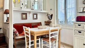 A dining area with a wooden table and chairs, a bench with red cushions, and a window with a view of buildings. - Charming and authentic fisherman's house, downtown and near the beach (Trouville-sur-Mer)