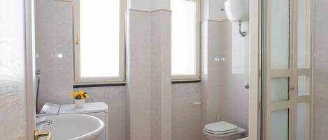 A bathroom with a sink, two toilets, a window, and a shower door.