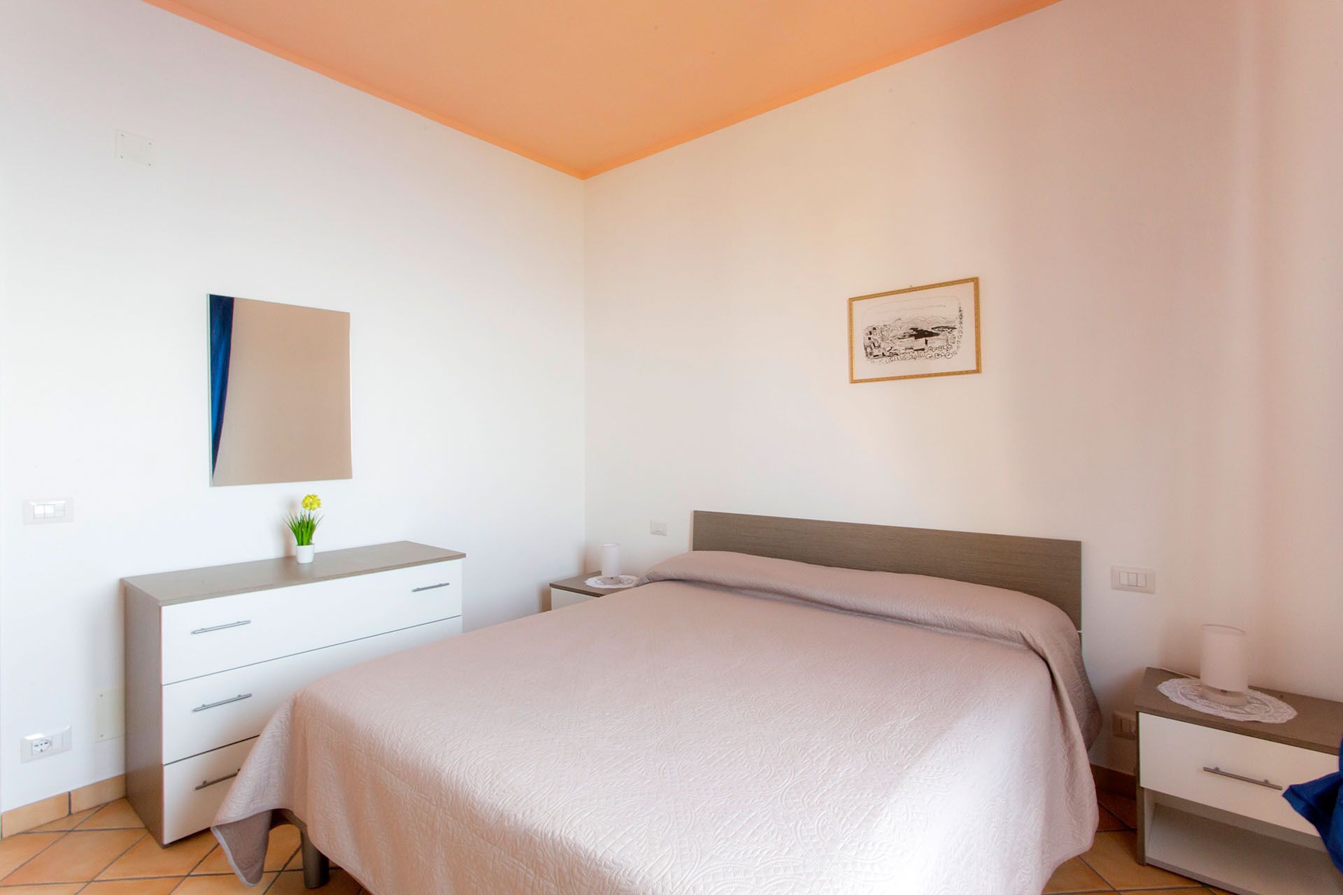 Une chambre à coucher comprenant un lit, une commode, une table de chevet, un miroir et un tableau encadré accroché au mur.