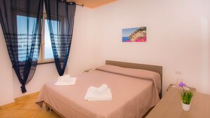 Ein Schlafzimmer mit einem Bett, zwei Handtüchern, einem kleinen Tisch mit Pflanze und einem Bild an der Wand.