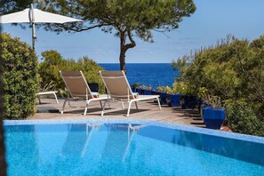 Ein Swimmingpool mit Liegestühlen und Blick aufs Meer.
