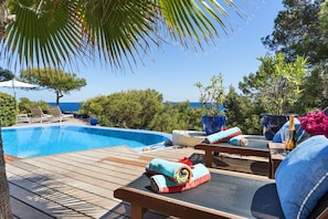 Ein Poolbereich mit Liegestühlen, einer Holzterrasse und Meerblick.