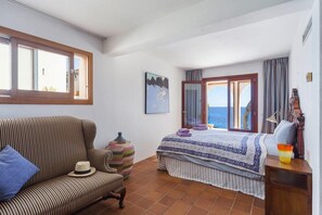 A bedroom with a bed, a chair, a window, a painting, and a view of the sea. - Front-Line Sea Villa In Mallorca. Up to 6 Guests (Capdepera)