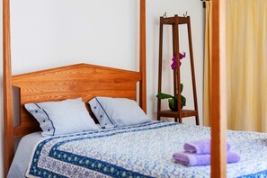 Un lit avec une tête de lit en bois, une couvre-lit à motifs et une table de chevet sur laquelle est posée une plante en pot.