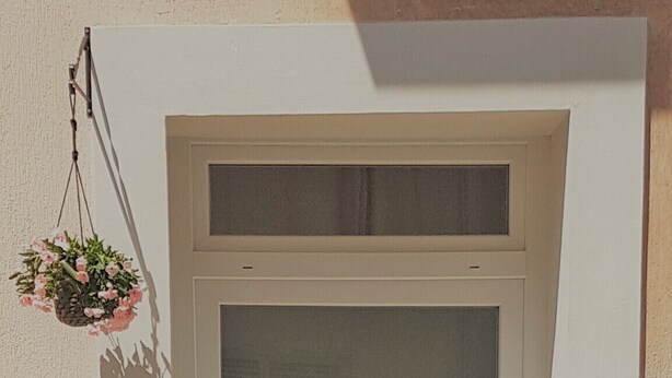 Una puerta blanca con un panel de vidrio esmerilado, una pequeña ventana arriba de la puerta y una maceta colgante a la izquierda.