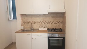 Una cocina compacta con gabinetes blancos, un lavamanos de acero inoxidable, una estufa a gas y un horno empotrado.