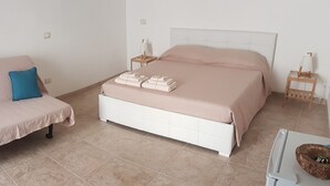 Un dormitorio con cama, sofá y una pequeña mesa con lámpara.