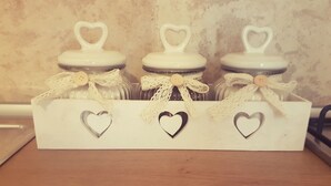 Una caja blanca con tres frascos, cada uno decorado con una tapa en forma de corazón y lazos de encaje.