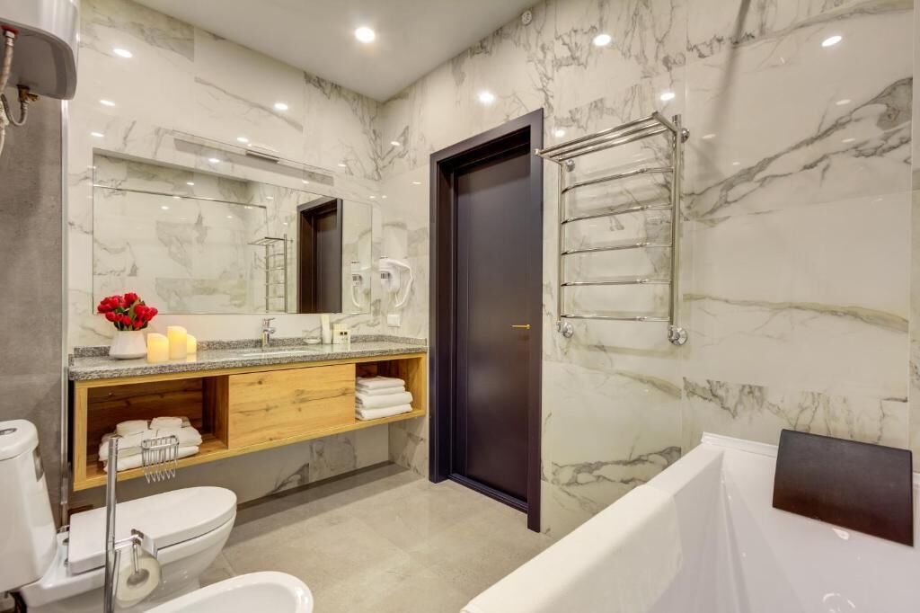 Ein modernes Badezimmer mit Marmorfliesenspiegel, einem Holzbadezimmermöbel, einer dunklen Tür und einer Glasdusche.
