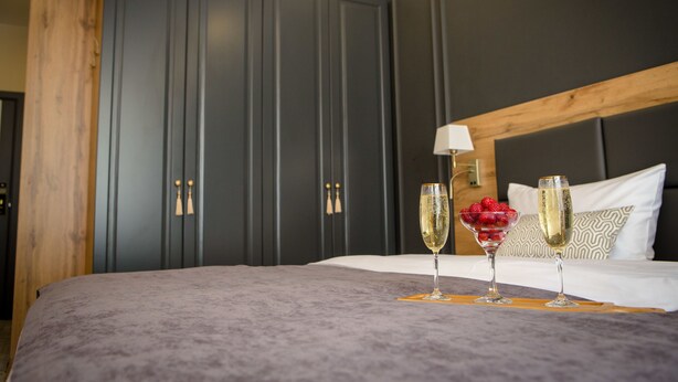 A neatly made bed with a grey blanket, two champagne glasses, and a bowl of strawberries. - Aurum Hotel (Bishkek)