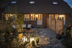 Une charmante maison de campagne avec un toit en tuiles, une clôture en bois et une terrasse en gravier aménagée avec du mobilier d’extérieur.