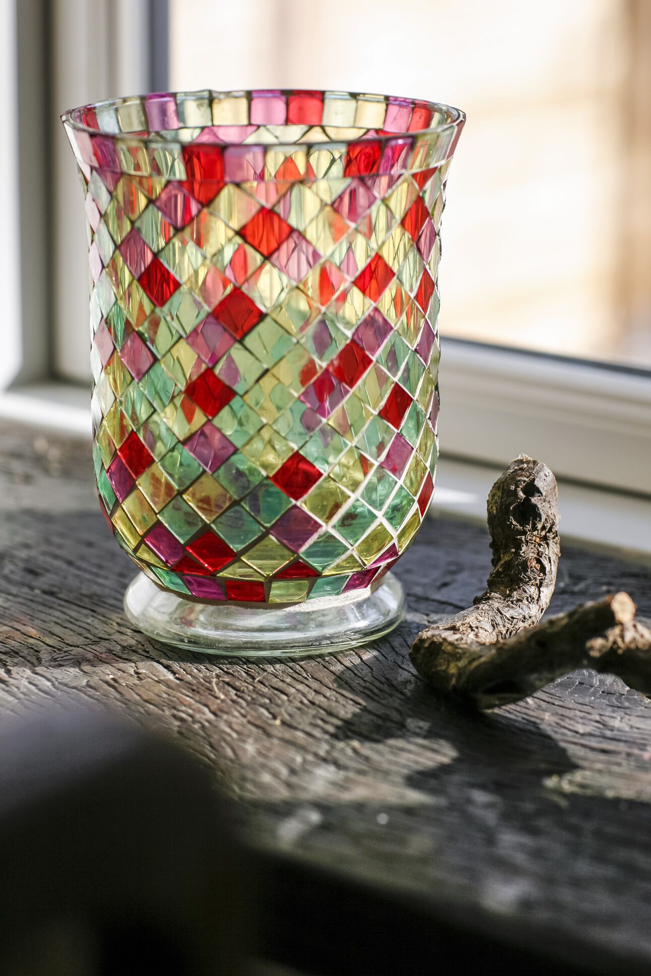 Eine mit Buntglas versehene Schale mit geometrischem Muster auf einer Holzoberfläche neben einem Zweig.