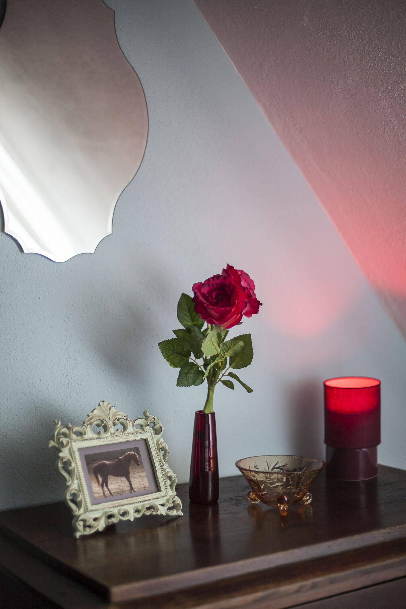 Une table en bois sur laquelle se trouve un tableau encadré, un vase avec une rose rouge, une bougie et un bol en verre.