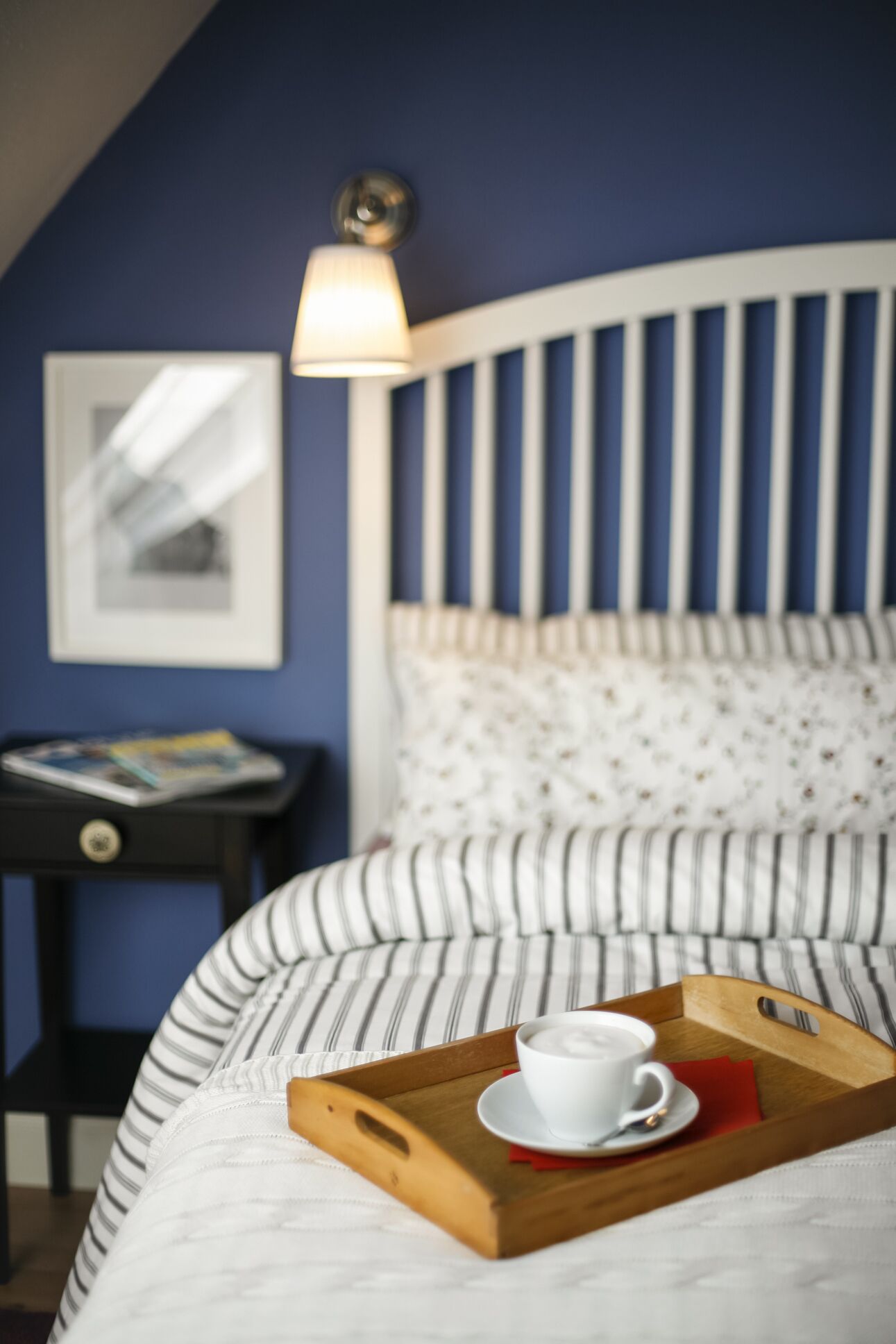 En snyggt bäddad säng med en randig kudde och ett brickbord med en kopp kaffe.