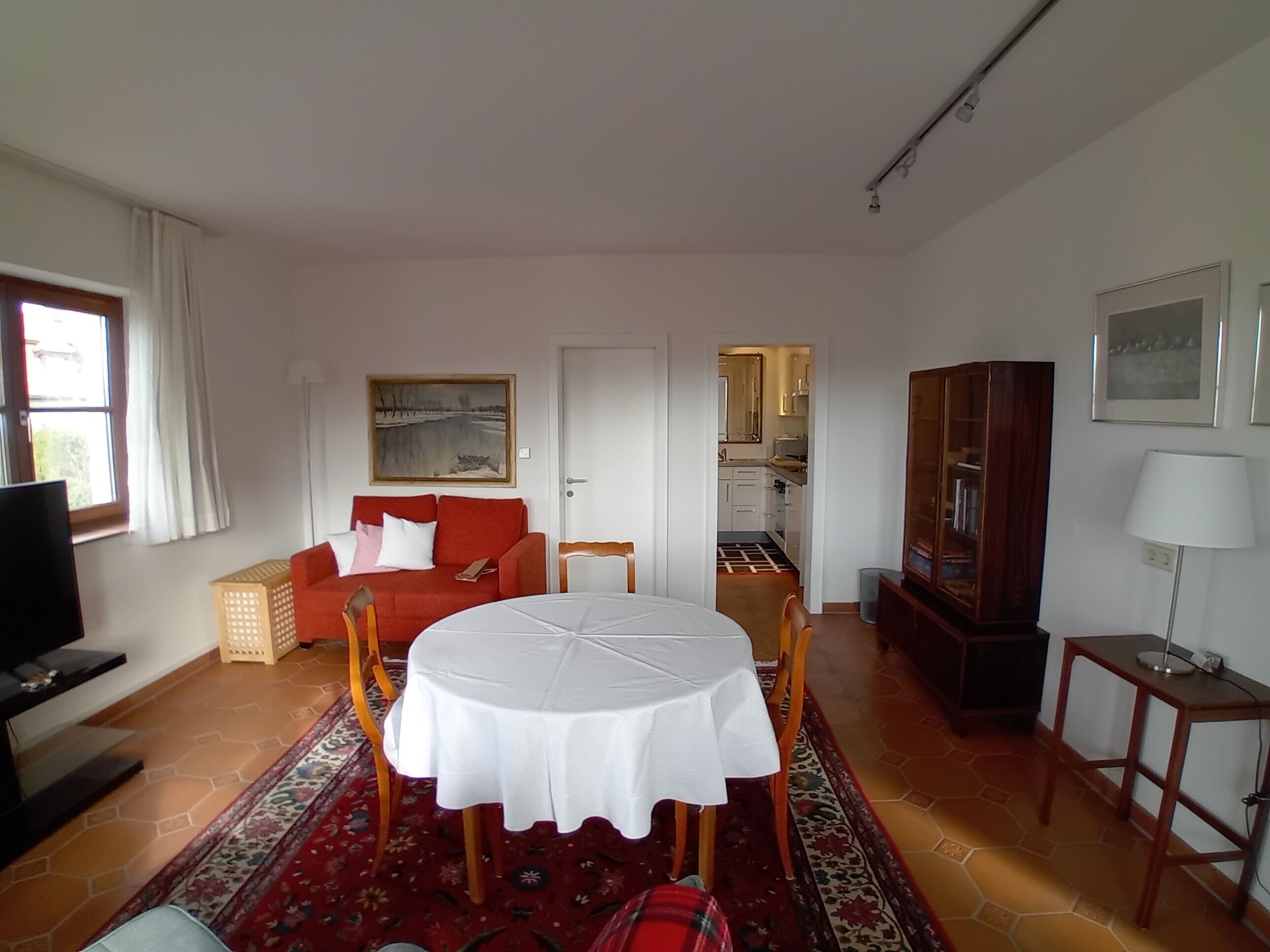 Ein Wohnzimmer mit rundem Tisch, rotem Sofa und einer Küche im Hintergrund.