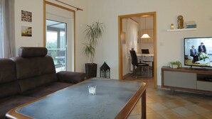 A living room with a sofa, a coffee table, a TV, and a dining area with chairs and a table. - Vacation home Gala in the vacation village Altes Land - Holiday home 303 Gala 80sqm for max. 6 persons (Hollern-Twielenfleth)