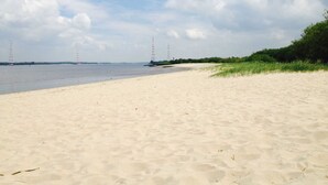 A sandy beach with a calm body of water, distant power lines, and greenery along the shore. - Vacation home Gala in the vacation village Altes Land - Holiday home 303 Gala 80sqm for max. 6 persons (Hollern-Twielenfleth)