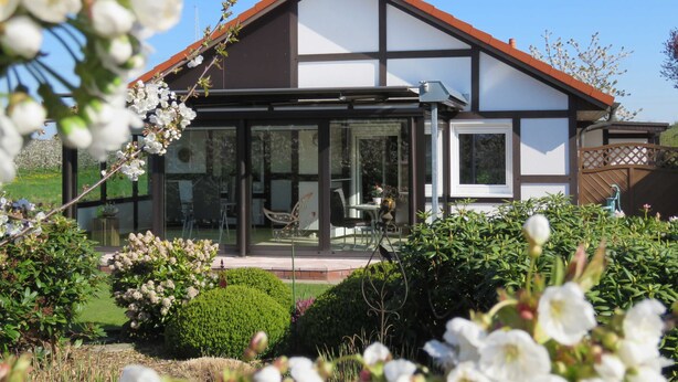 A modern house with a glass conservatory, surrounded by well-maintained gardens and flowering plants. - Vacation home Gala in the vacation village Altes Land - Holiday home 303 Gala 80sqm for max. 6 persons (Hollern-Twielenfleth)